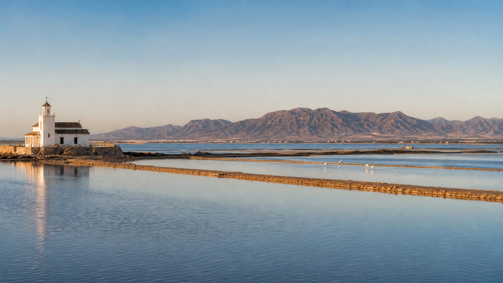 The church of the Salinas de Cabo de Gata reflected in the water, with flamingos in the foreground